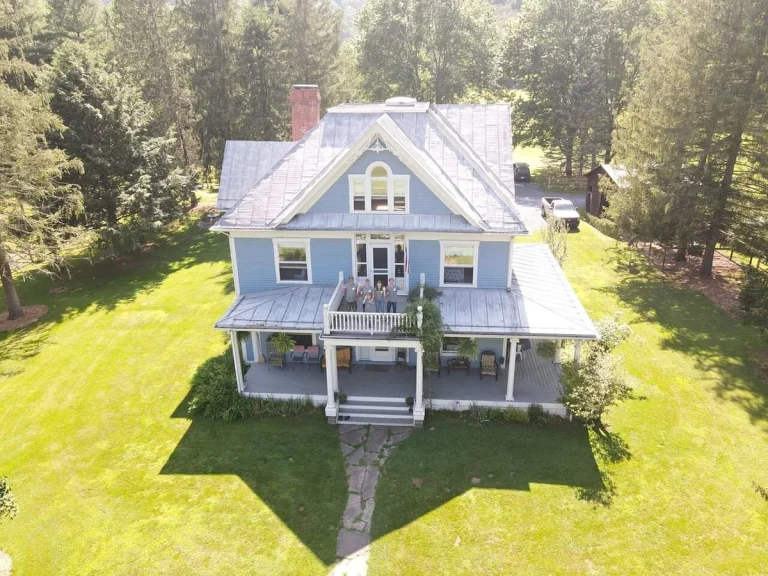Luchtfoto van een blauw victoriaans huis met veranda en balkon, omgeven door groen gazon en bos in West Virginia