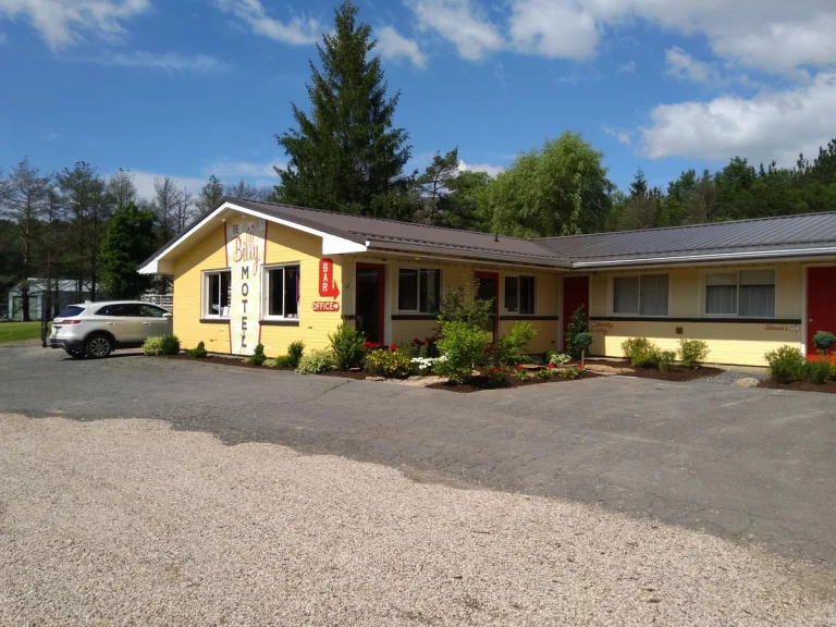 Een geel motelgebouw met rode deuren en een oprit van grind, omgeven door bomen en bloemperken in West Virginia