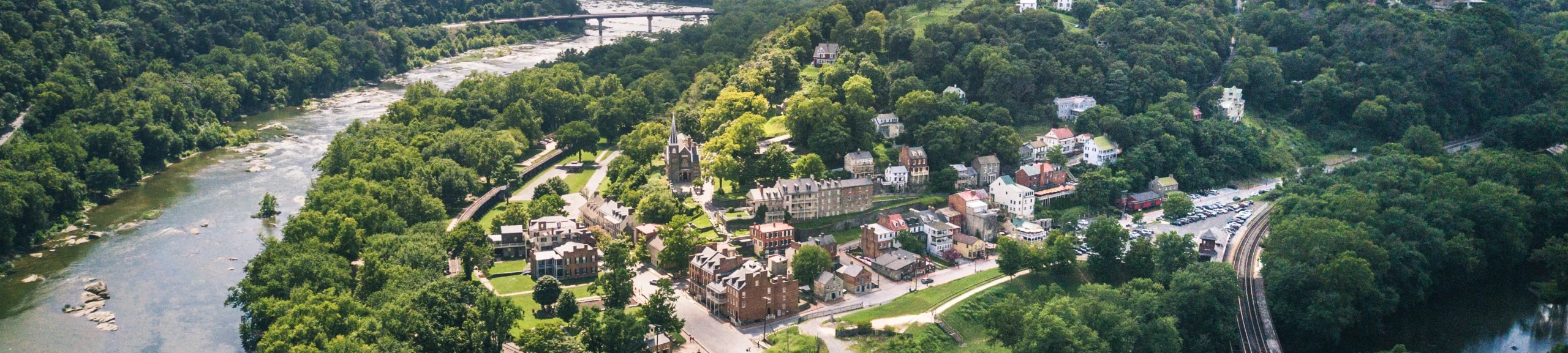 Vanuit de lucht gezien liggen kleine huizen en een kerktoren tussen dicht bos aan een brede rivier in West Virginia