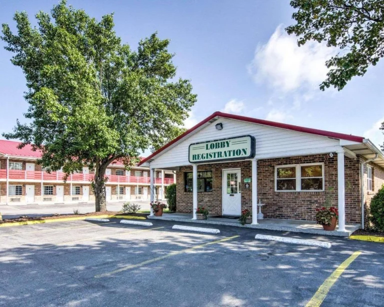 Een bakstenen motelgebouw met rood dak en een bord met lobby en registratie, gelegen aan een lege parkeerplaats in West Virginia