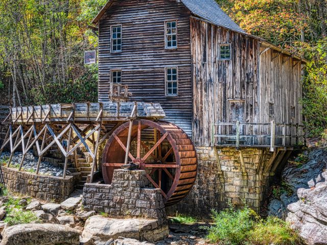 Een verweerde houten watermolen met groot roestig waterrad staat naast een stenen goot in de bossen van West Virginia