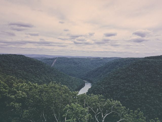 Een kronkelende rivier stroomt tussen dichtbegroeide, groene heuvels onder een bewolkte lucht in West Virginia