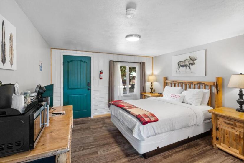 Slaapkamer met een houten bed, een groene deur en een schilderij van een eland aan de muur in een rustieke cabin