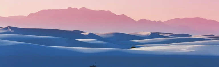 Golvende witte gipsduinen van White Sands National Park onder een roze avondlucht met een lange bergketen op de achtergrond
