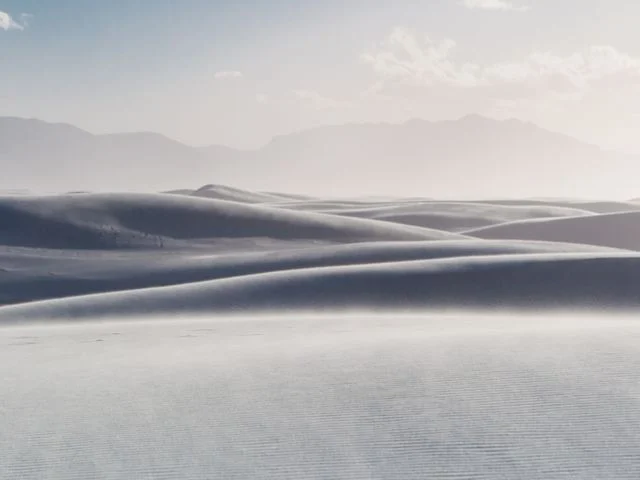 Golvende witte gipsduinen van White Sands National Park met een waas van opwaaiend zand en bergen op de achtergrond