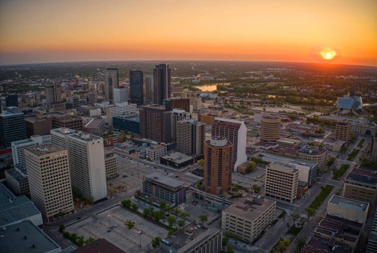 Luchtfoto van hoge gebouwen in het centrum van Winnipeg met een rivier en oranje avondlucht op de achtergrond