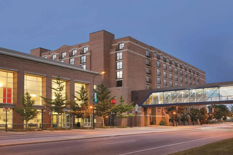 Groot bakstenen hotelgebouw met een overdekte loopbrug over de straat, verlicht bij het vallen van de avond in Wisconsin