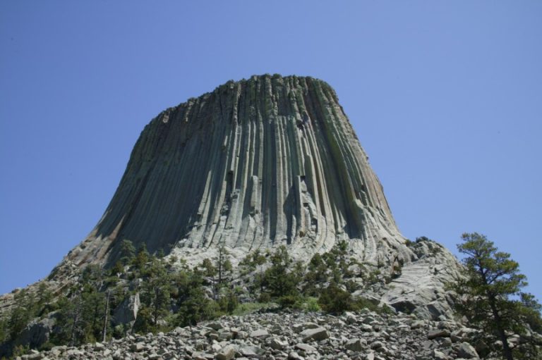 De karakteristieke verticale groeven van Devils Tower gezien vanaf de voet met rotsblokken en dennenbomen eromheen