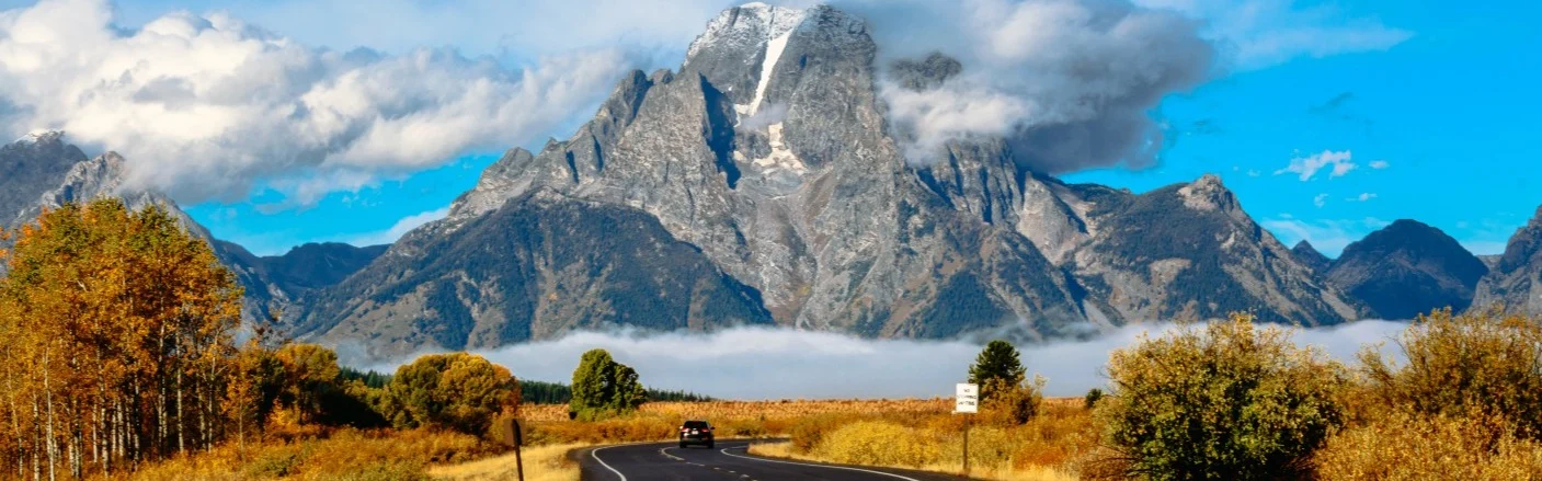Groot bord langs de weg met de tekst Welcome to Wyoming Forever West en een afbeelding van een cowboy op een steigerend paard tegen een blauwe lucht