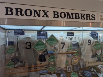 Museumvitrine met vergeelde honkbalshirts met de nummers drie zeven en negen en informatiepanelen over Yankees legendes