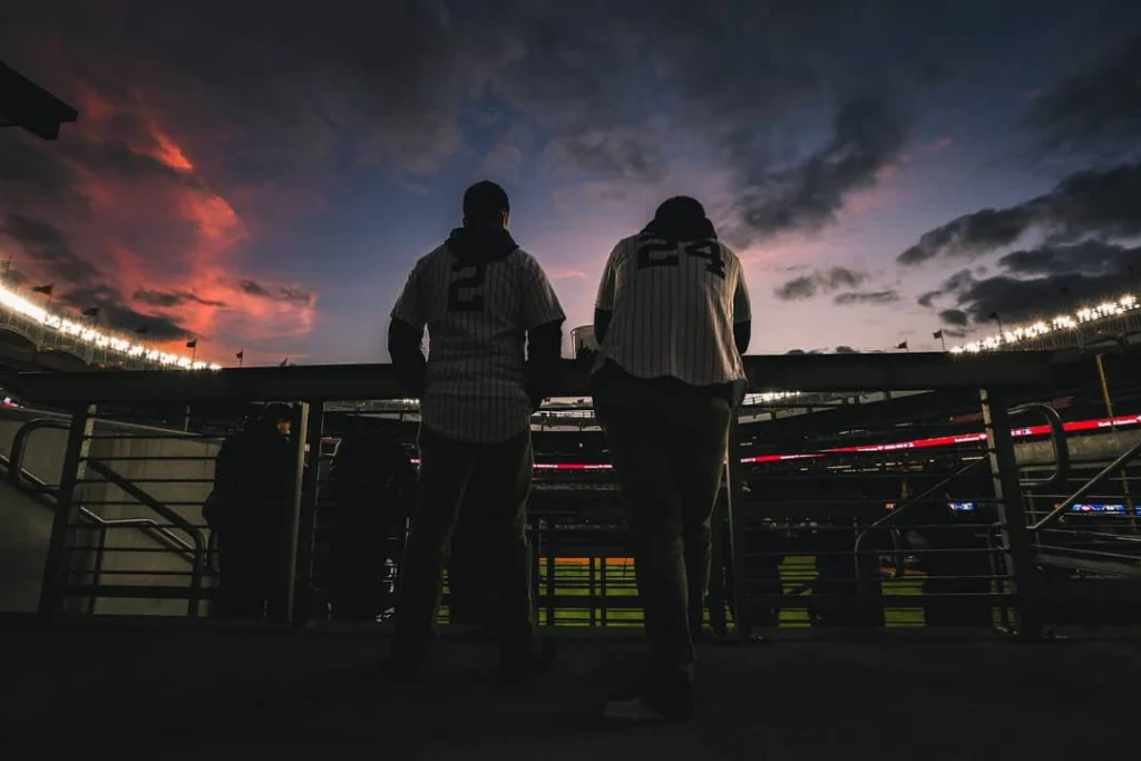 Twee fans in pinstripe shirts kijken bij zonsondergang uit over het stadion met een roze gekleurde lucht