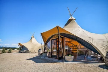 Rij grote beige tenten met puntige toppen en glazen gevels op een kale vlakte onder een strakblauwe hemel