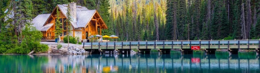 Houten lodge met houten brug over turquoise meer omringd door dennenbos in Yoho National Park