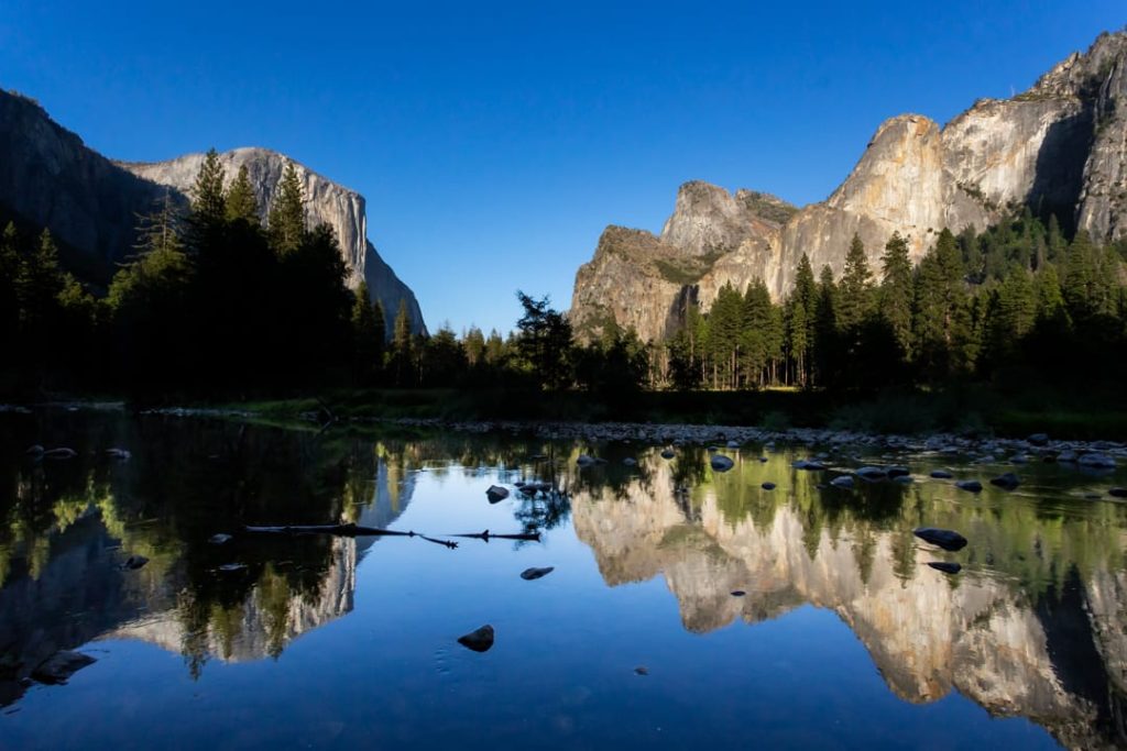 Granieten rotswanden van Yosemite Valley weerspiegelen in het spiegelgladde water van de Merced River bij zonsopgang