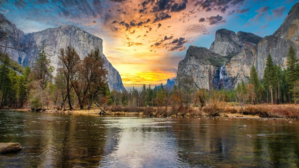 Kleurrijke zonsondergang boven de rivier in Yosemite Valley met steile granieten rotswanden en bomen langs de oever