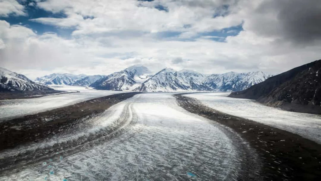 Luchtfoto van een brede gletsjer die tussen besneeuwde bergtoppen door een vallei stroomt in Yukon