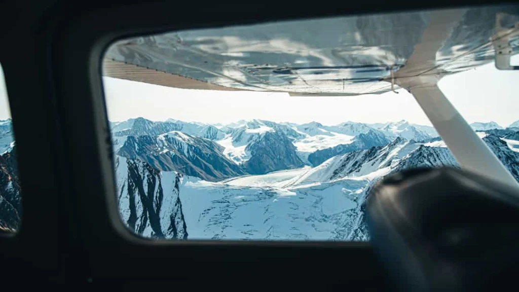 Uitzicht vanuit het raam van een klein vliegtuig met de vleugel zichtbaar over een besneeuwd gletsjerlandschap in Yukon