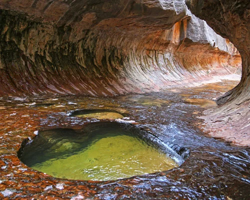 Groenig water stroomt door een ronde poel tussen gladgeslepen rode en witte rotswanden in de beroemde Subway van Zion National Park