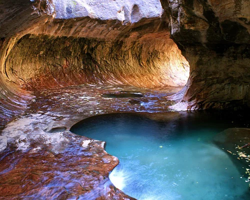 Helder turquoise water verzamelt zich in een ronde poel binnen de gladgeslepen rode rotswanden van The Subway in Zion National Park