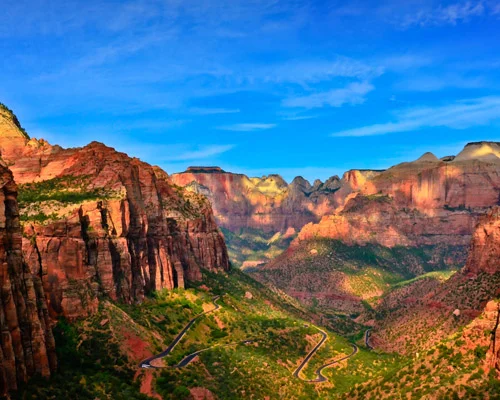 Panoramisch uitzicht op de kronkelende weg door de rode rotsformaties van Zion Canyon met groene vallei en bergen op de achtergrond