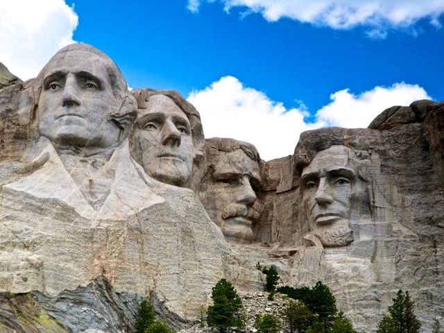 Close-up van de vier presidentskoppen van Mount Rushmore uitgehouwen in grijze granietrots tegen een blauwe lucht met wolken
