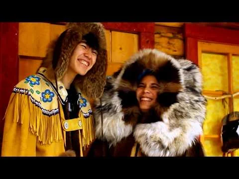 Twee lachende jonge inwoners van Alaska dragen traditionele kleding met kraaltjes en bontmutsen in een houten gebouw