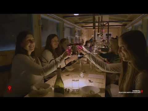 Groep vrouwen heft glazen wijn tijdens een diner in een restaurant in Churchill, met de tekst Frontiers North Adventures in beeld