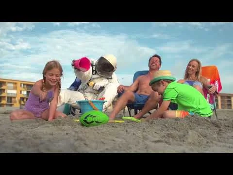 Een gezin met kinderen bouwt zandkastelen op het strand van Cocoa Beach terwijl een mascotte verkleed als astronaut meespeelt