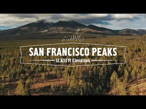 Videostilstaand beeld met de tekst San Francisco Peaks en de hoogte van 12633 voet over een luchtfoto van beboste heuvels en bergen bij zonsondergang