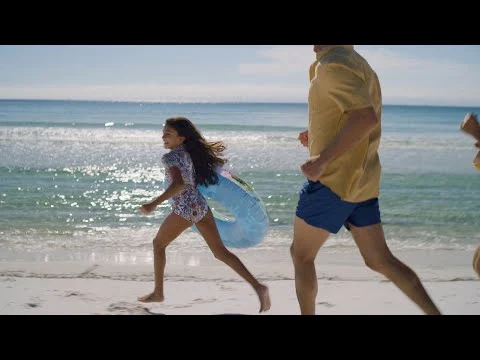 Videothumbnail van een vader en dochter die lachend over een zonnig strand rennen tijdens een fly drive door Florida