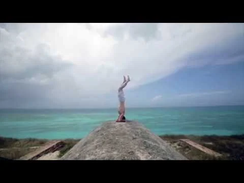 Een vrouw maakt een handstand op een rotsformatie met turquoise zee en bewolkte lucht op de achtergrond in Florida
