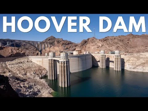 Videobeeld van de Hoover Dam gezien vanuit de lucht met de kenmerkende koeltorens, het blauwgroene water van het stuwmeer en de brug over de kloof