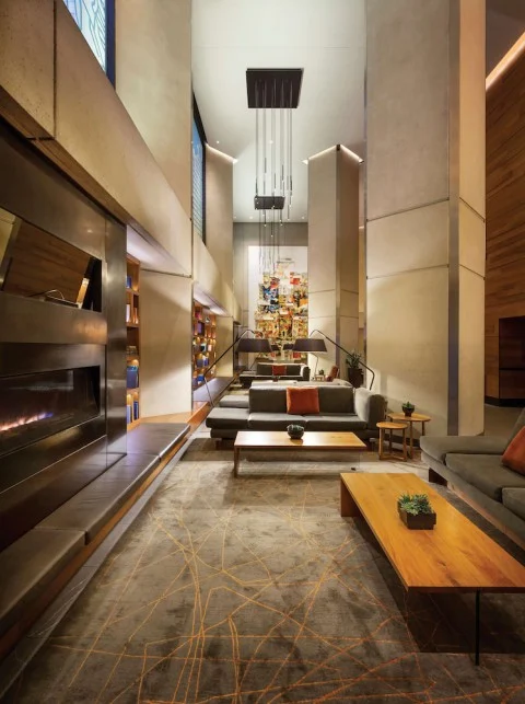 Moderne zithoek in een hotellobby met een lange open haard, grijze banken en kunst aan de hoge wand