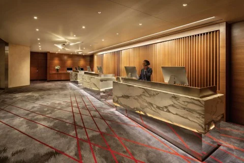Ruime hotellobby met een lange marmeren receptiebalie, houten lamellen op de wand en een medewerker achter de balie