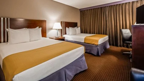 Hotelkamer met twee opgemaakte bedden met gele sprei, een nachtkastje met lamp en een bureau met stoel