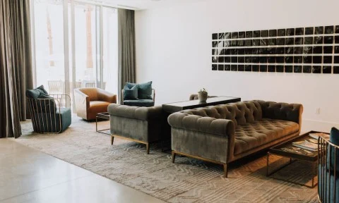 Moderne zithoek in een hotelkamer met een fluwelen bank, twee fauteuils en een rij kleine kunstwerken aan de muur