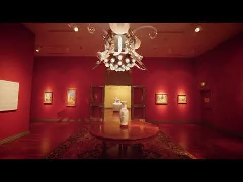 Een museumzaal in Huntsville met diepe rode wanden, kunstwerken en een sierlijke kroonluchter boven een ronde tafel