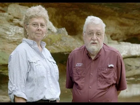 Man en vrouw op leeftijd staan naast elkaar voor een beige rotswand in een natuurgebied in Illinois