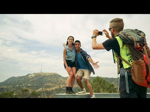 Man fotografeert een lachend stel op een uitkijkpunt met het Hollywood Sign zichtbaar op een heuvel in de verte