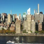 Luchtfoto van hoge appartementengebouwen en kantoortorens van Manhattan langs de oever van de rivier, met een bootje op het water