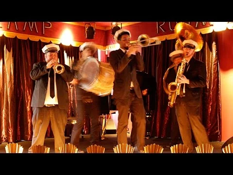 Vier muzikanten in pak spelen trompet, trombone en saxofoon op een podium met rode gordijnen in New Orleans