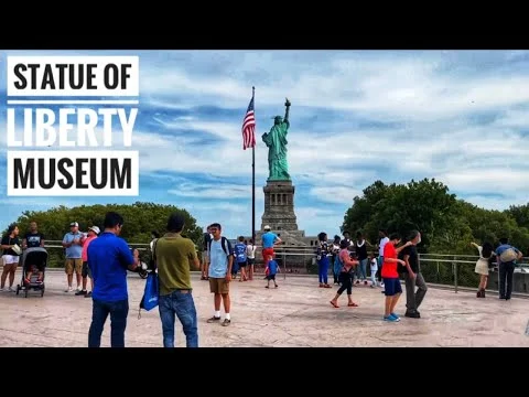 Videothumbnail met de tekst Statue of Liberty Museum en bezoekers op een plein met uitzicht op het Vrijheidsbeeld