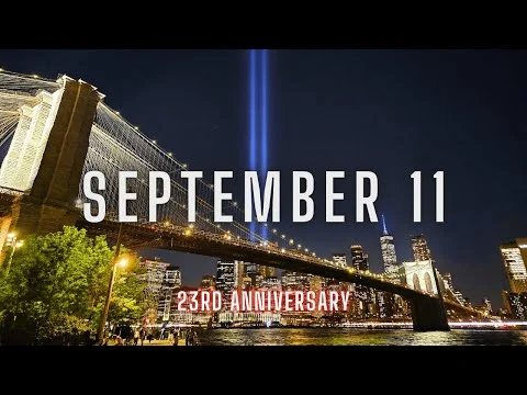 Verlichte Brooklyn Bridge in de avond met op de achtergrond de twee lichtbundels van de Tribute in Light