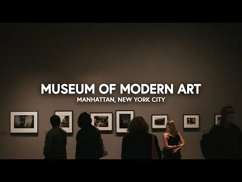 Videostill van een donkere galerie met bezoekers bij fotolijsten aan de wand, met de tekst Museum of Modern Art Manhattan New York City in beeld
