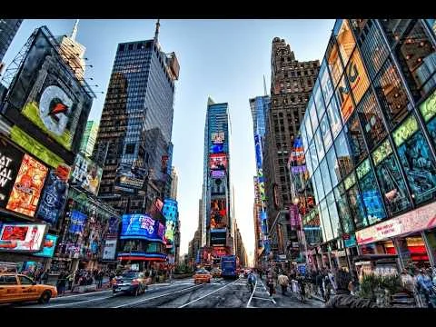 Videothumbnail met een breedhoekopname van Times Square overdag met gele taxi's, voetgangers en reclameborden aan weerszijden van de straat