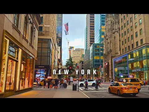 Videostill van een levendige straat in New York met gele taxi's, voetgangers en hoge gebouwen, met de tekst New York in beeld