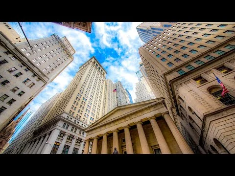 Videobeeld van omhoog gefotografeerde wolkenkrabbers rond Wall Street met de zuilengevel van Federal Hall onderin beeld