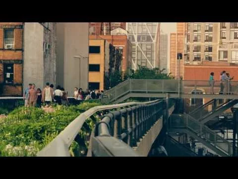 Wandelaars lopen over het beplante pad van de High Line tussen bakstenen gebouwen en trappen in New York bij avondlicht