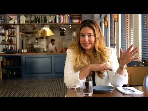 Videobeeld van een lachende vrouw aan een tafel die praat, met een open keuken op de achtergrond in een restaurant in Rhode Island