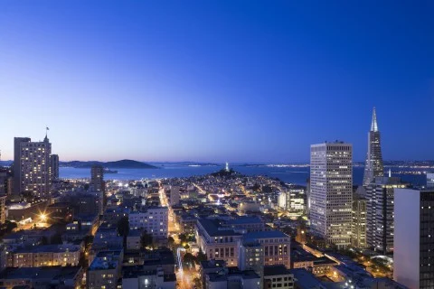 Verlichte skyline van San Francisco bij blauw uur met de spitse Transamerica Pyramid en de baai op de achtergrond